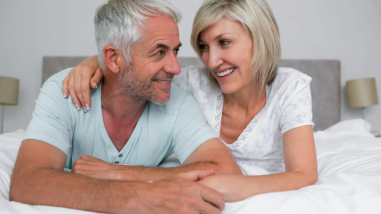 A smiling older couple lying on a bed and looking at each other