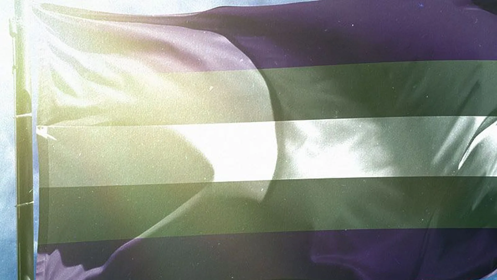 A striped pride flag waving against a bright cloudy sky