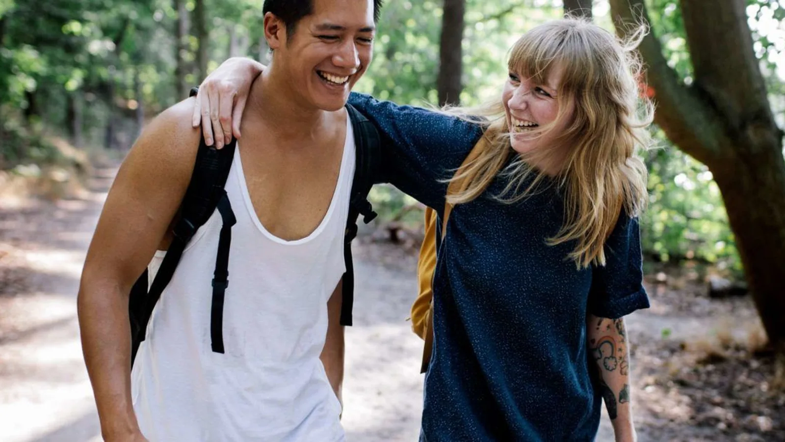 A laughing couple walking arm in arm along a forest path