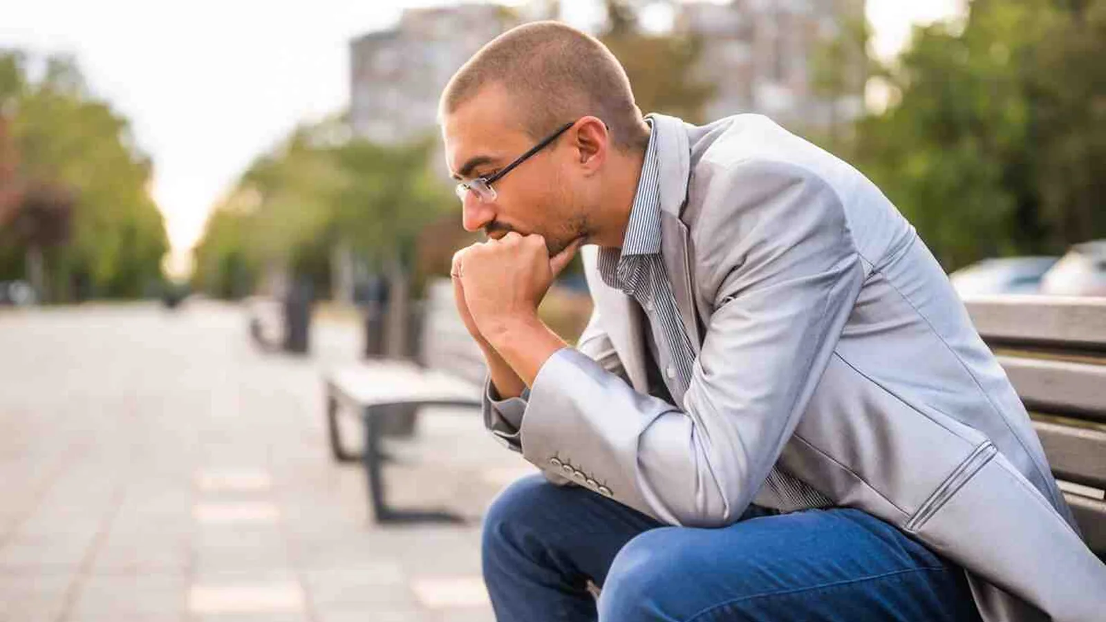 A man sitting on a park bench with his chin on his hand, deep in thought