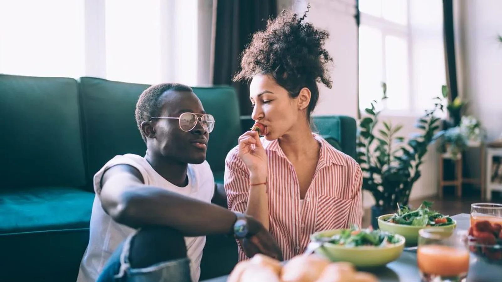 A couple sharing a meal and laughing together on a sofa at home