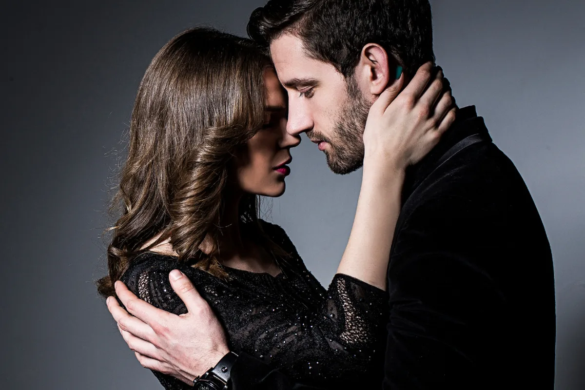 A couple in dark clothes embracing with foreheads close together