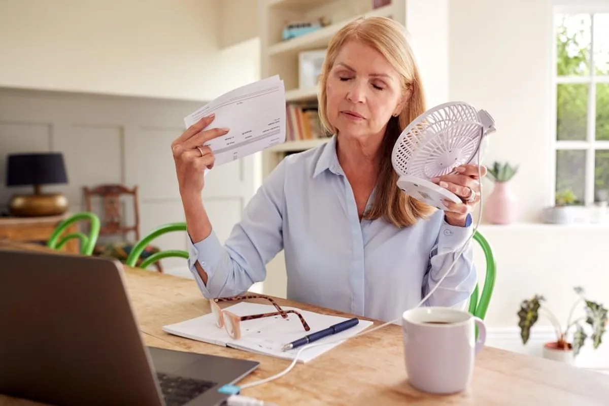 A woman at her desk cooling herself with a small handheld fan