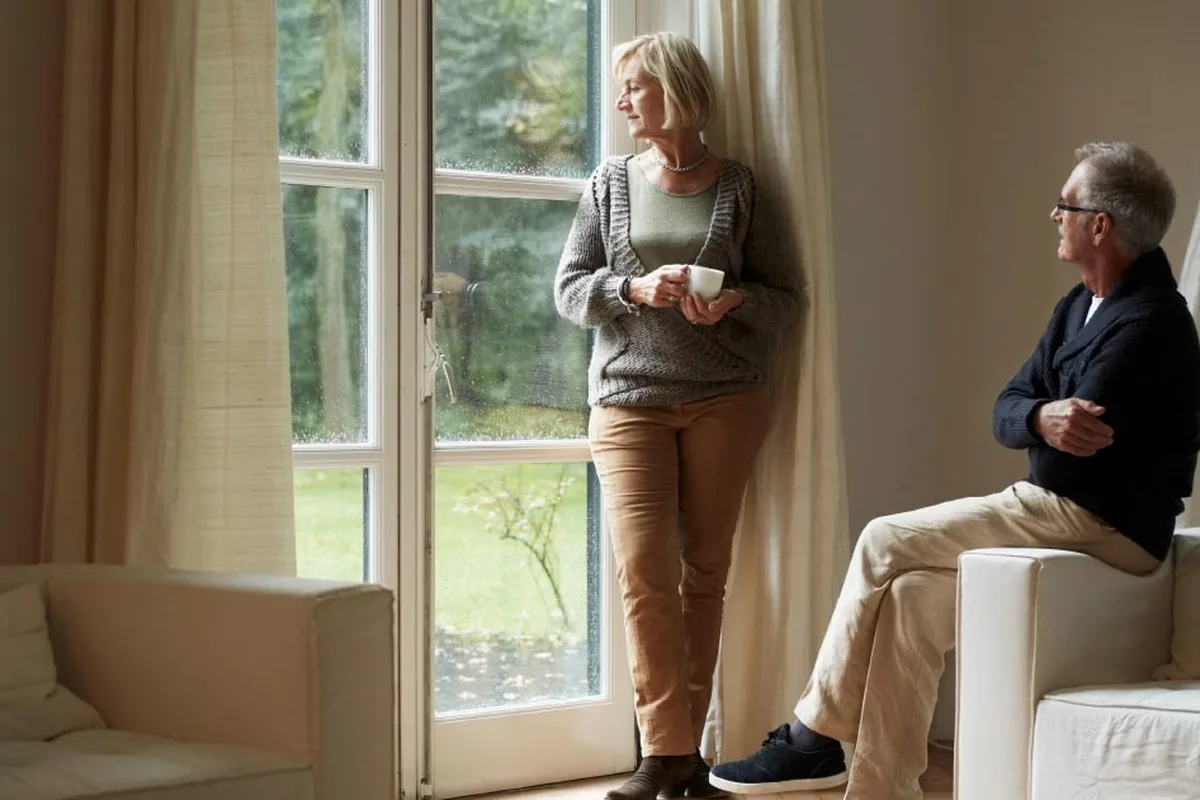 An older couple at home looking out of different windows