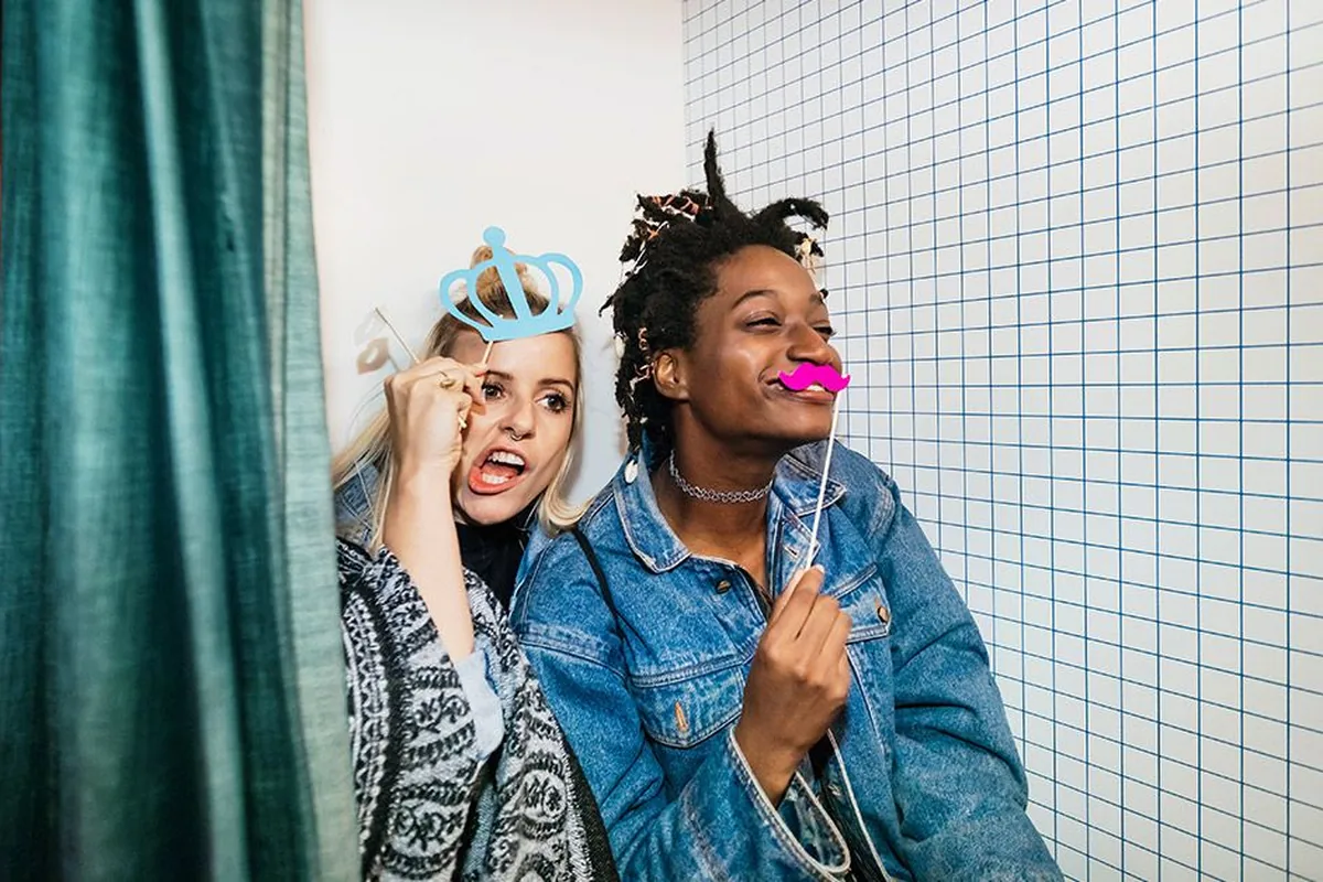 Two friends pulling faces with photo-booth props