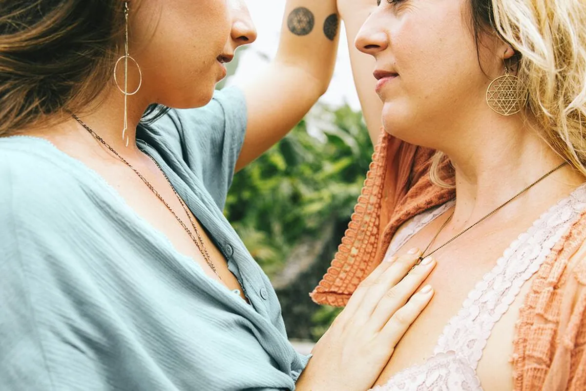 Two women standing close together outdoors, one resting a hand on the other’s chest