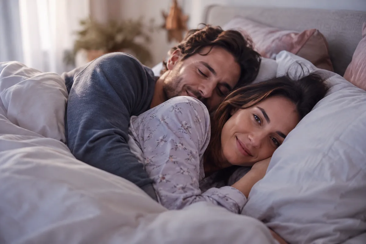 A couple in pajamas lying close under a duvet, one spooning the other