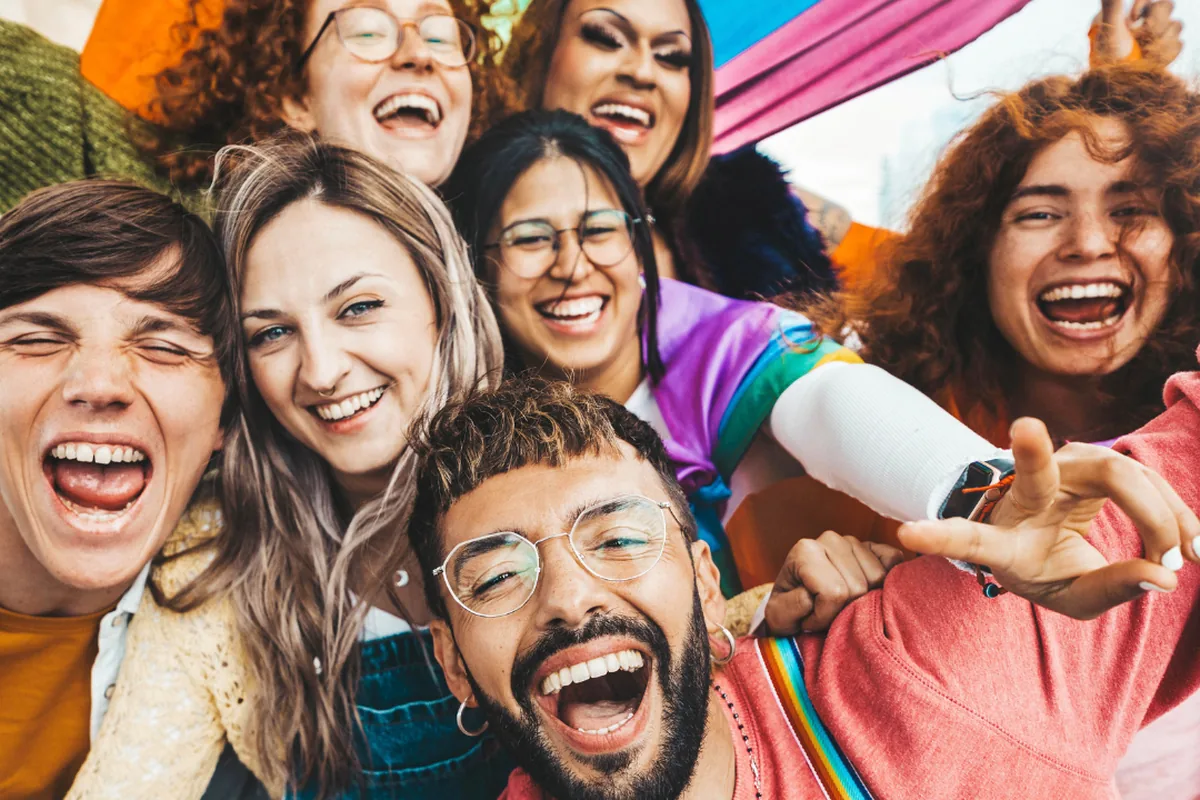 A laughing group of friends with pride flags taking a selfie