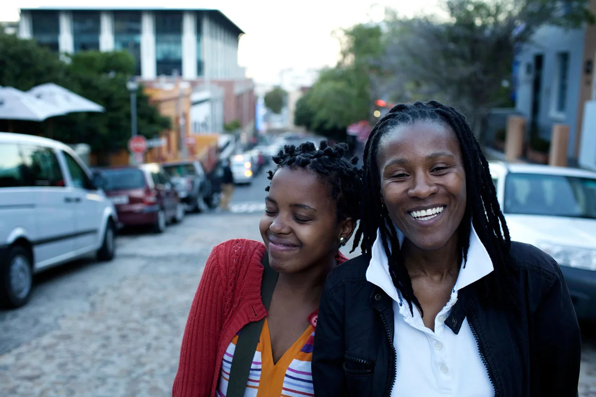 Two smiling women standing close together on a city street