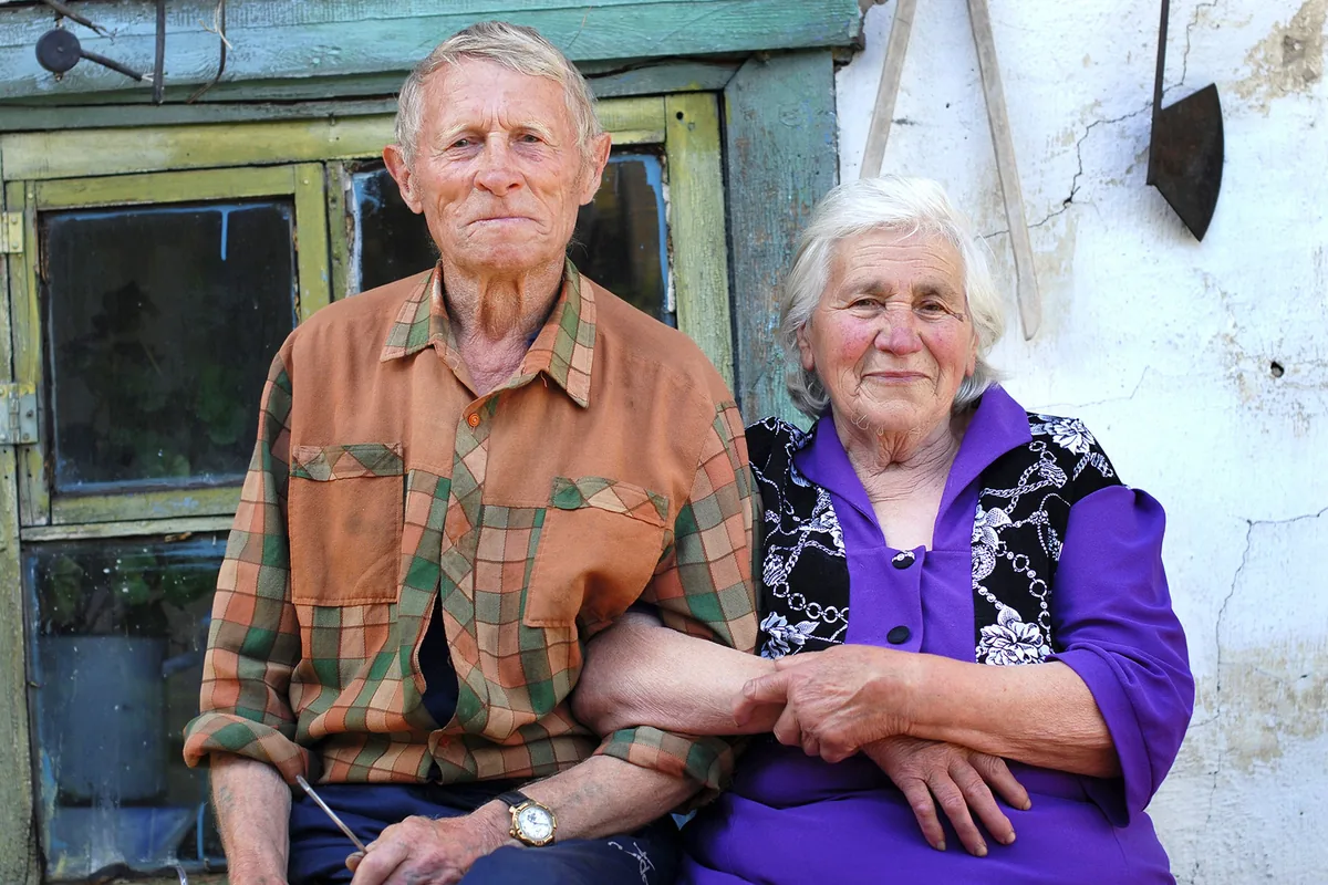 An elderly couple sitting arm in arm outside their house