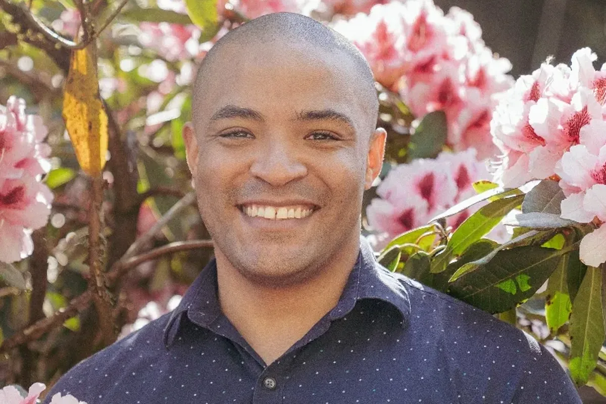 A smiling man standing in front of a flowering shrub