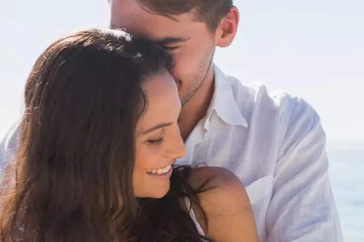 A couple embracing on a beach, the man hugging the woman from behind
