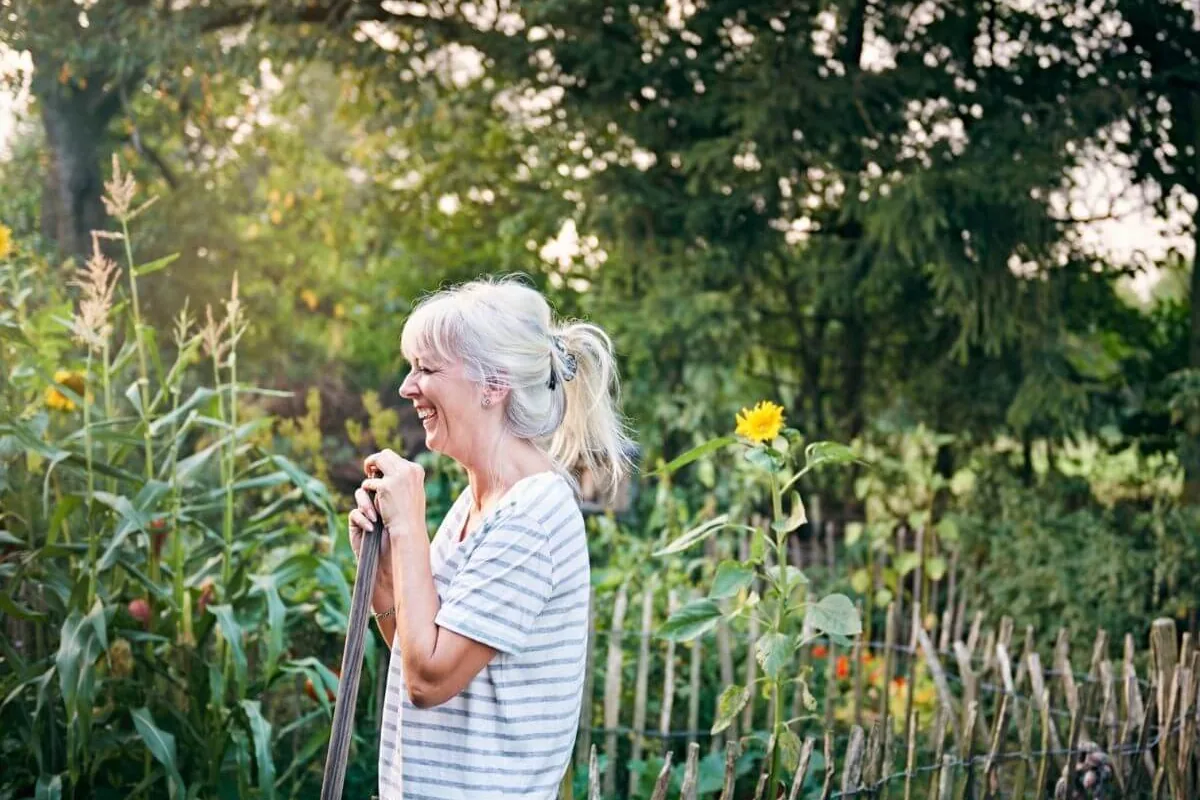 A smiling older woman standing in a sunlit vegetable garden