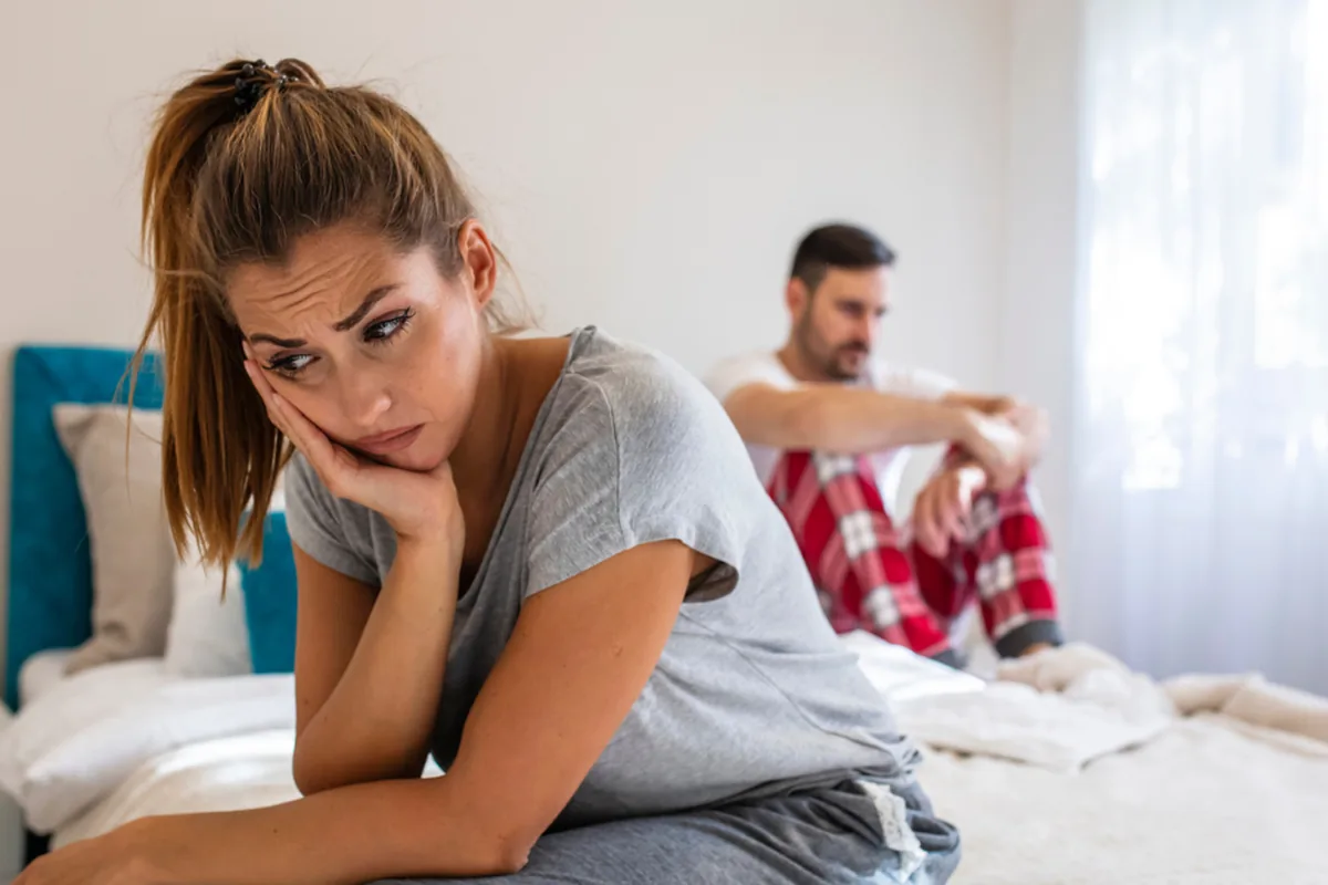 A frustrated woman sitting on the bed while a man sits behind her