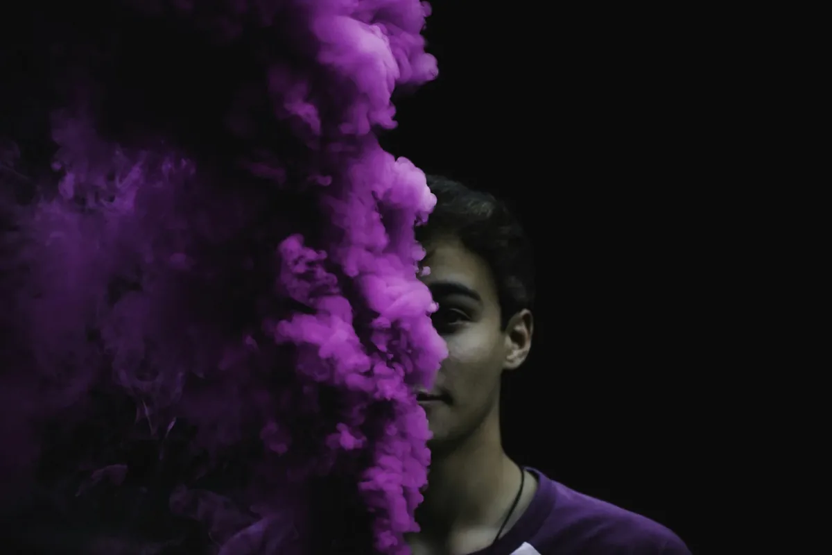 A young man’s face half hidden by a cloud of purple smoke