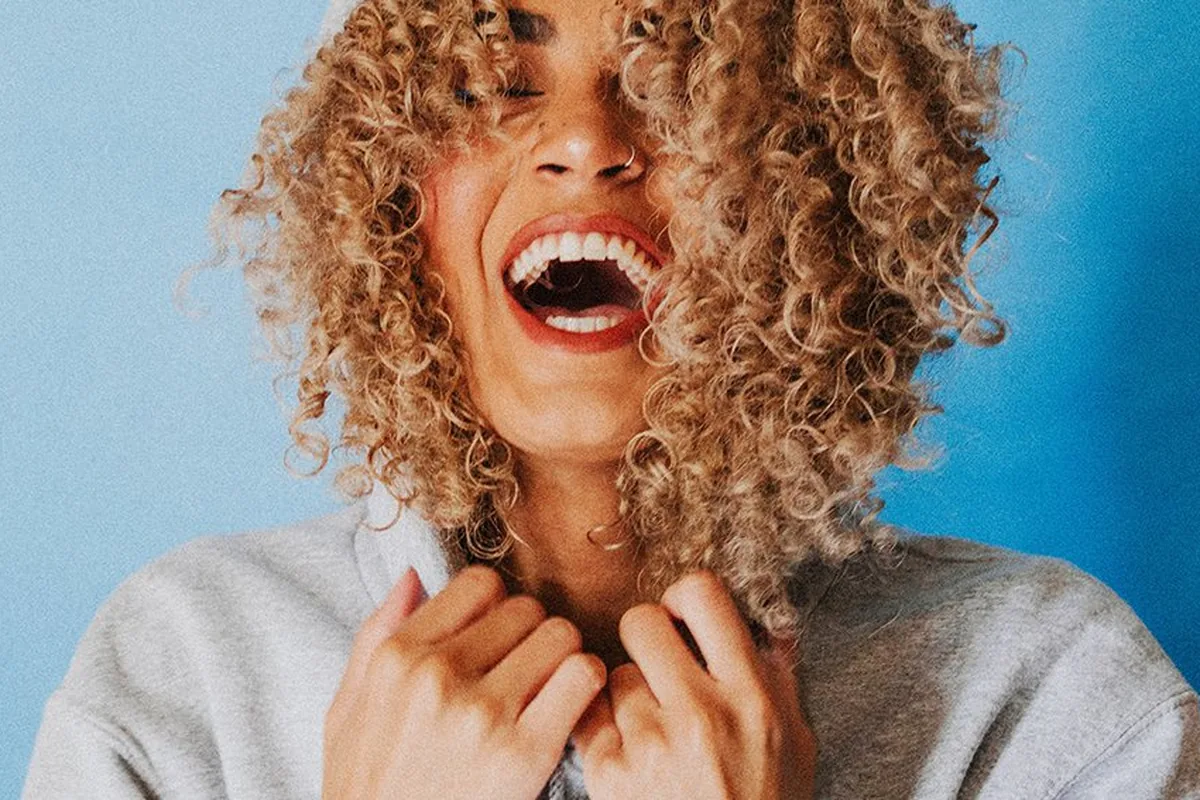 A woman with curly hair laughing with her eyes closed
