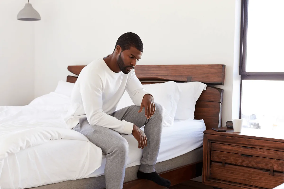 A man sitting on the edge of his bed looking down, deep in thought