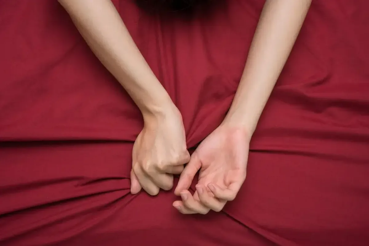 Two hands gripping a deep red bedsheet