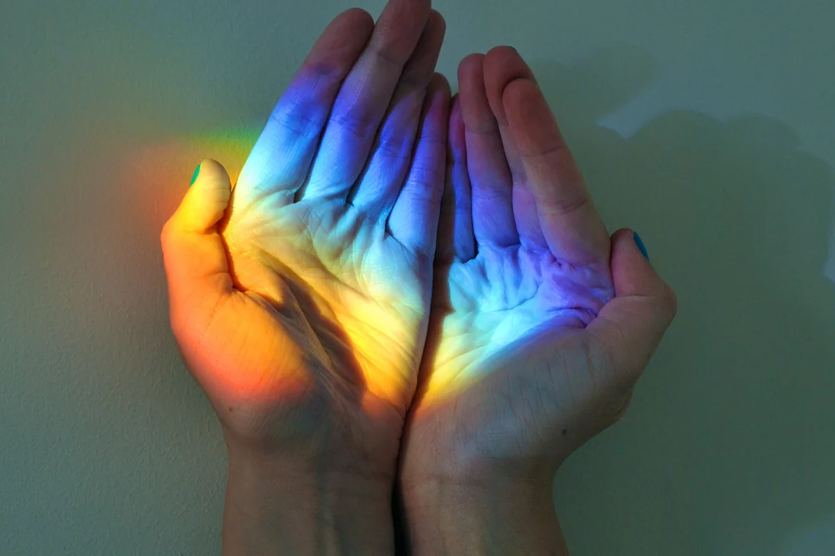 Cupped hands holding a patch of rainbow-coloured light