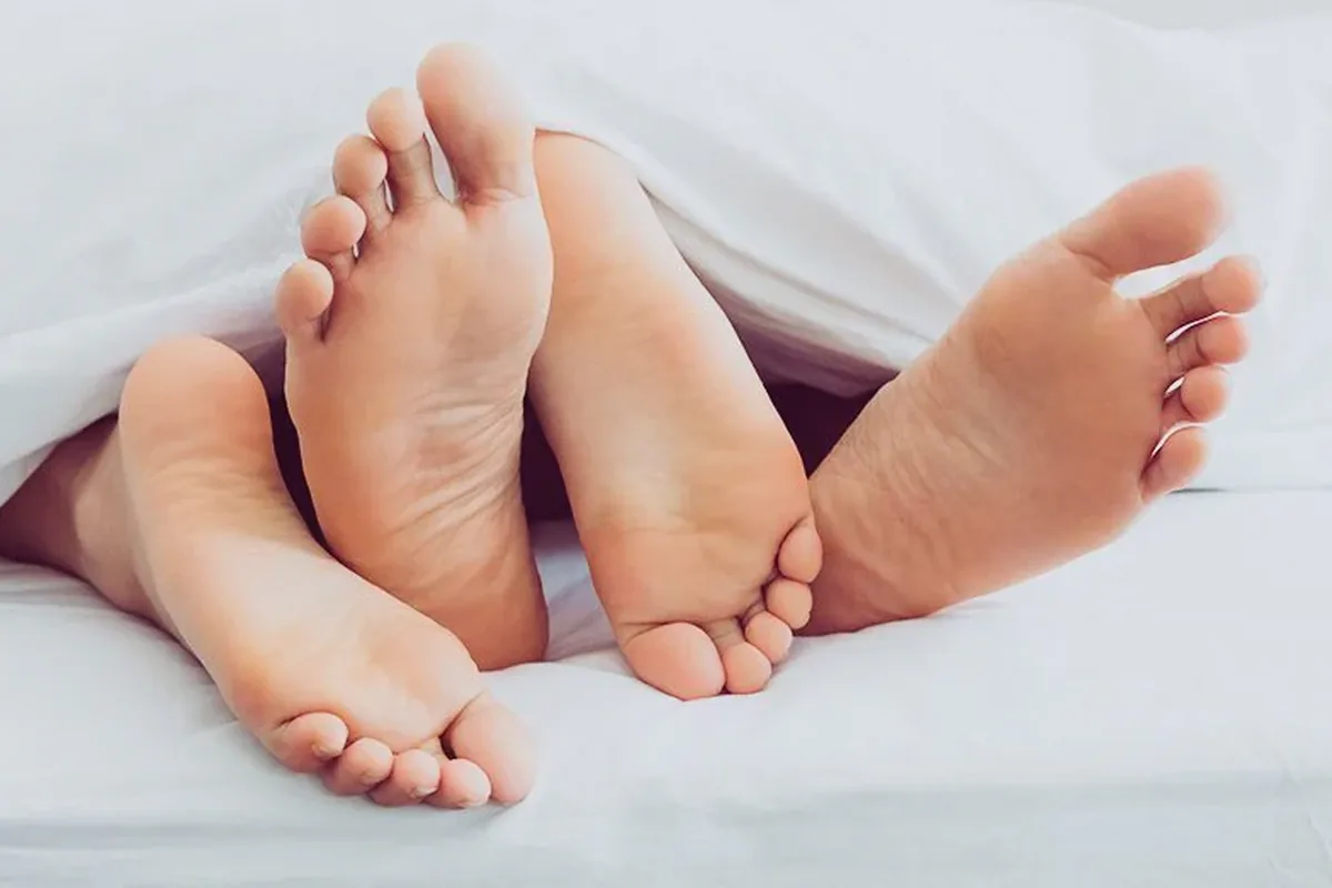 Two pairs of bare feet peeking out from under a white duvet