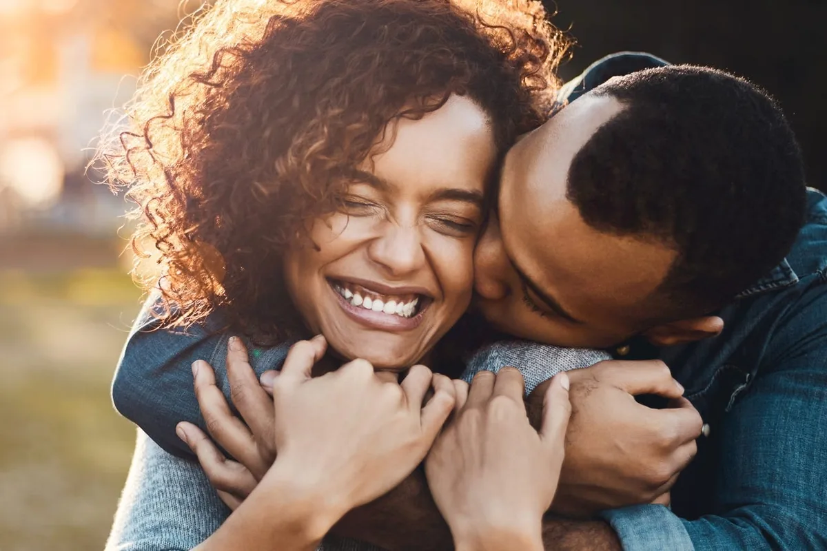 A laughing woman embraced by her partner, who kisses her cheek