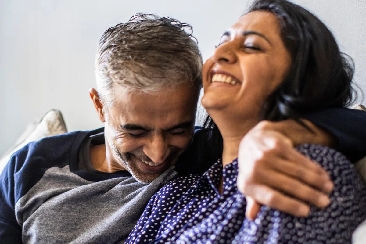 A middle-aged couple laughing together on a sofa