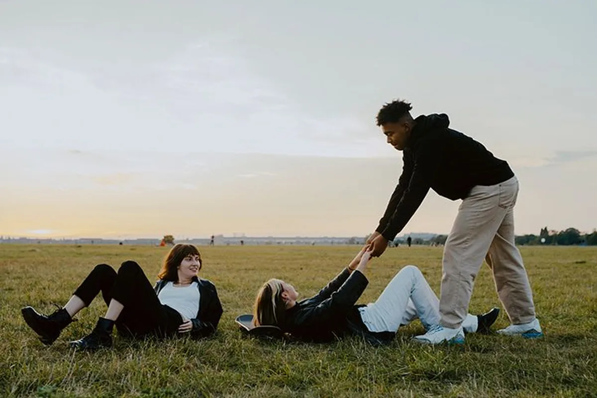 Friends lying in a field while one helps another up