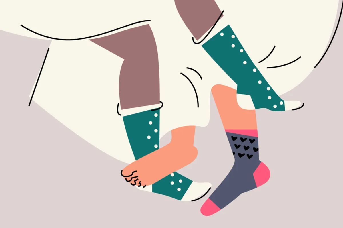 Colorful flat illustration of two pairs of legs tangled together in bed, one wearing teal polka-dot socks and the other a heart-patterned sock