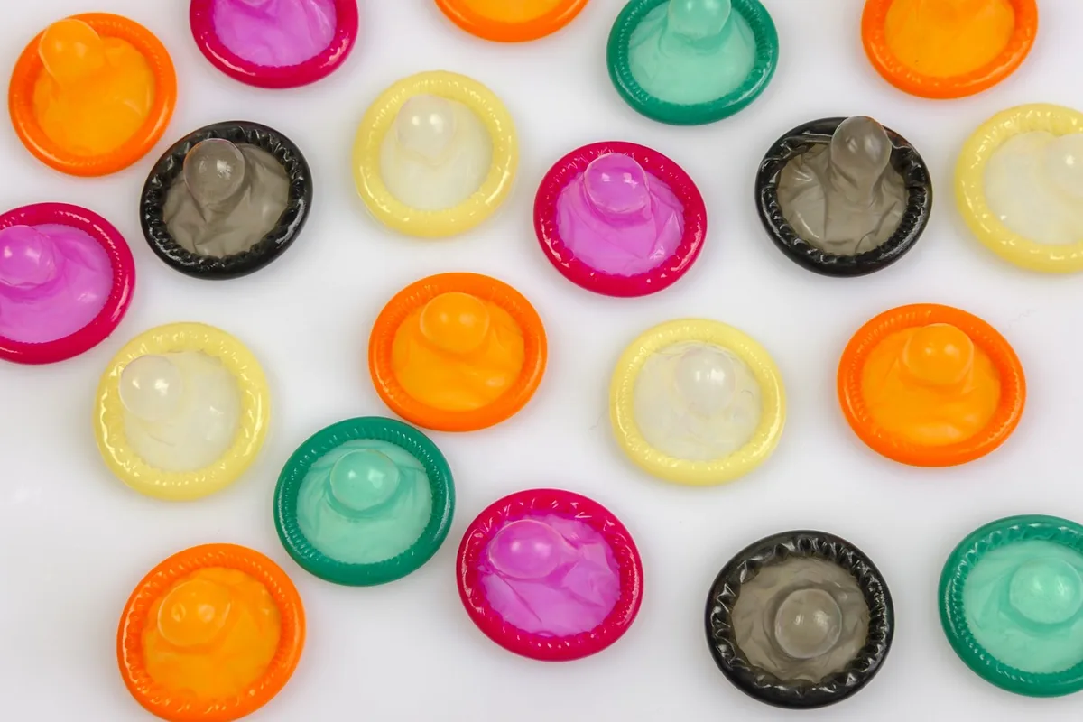 Colorful rolled condoms scattered on a plain white surface, photographed from above
