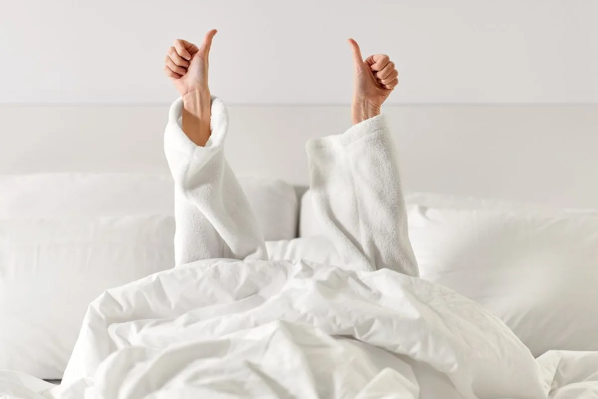 Two arms in white sleeves giving thumbs up from under a duvet