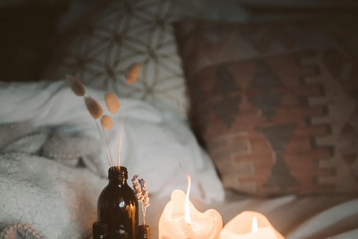 Lit candles and a small bottle on a tray on an unmade bed