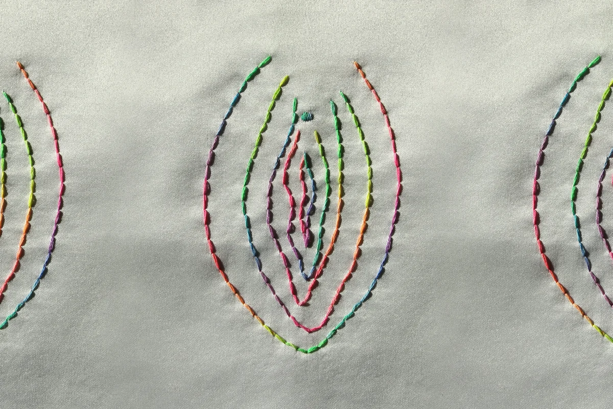 Embroidery of a vulva outline stitched in rainbow-coloured thread on pale fabric