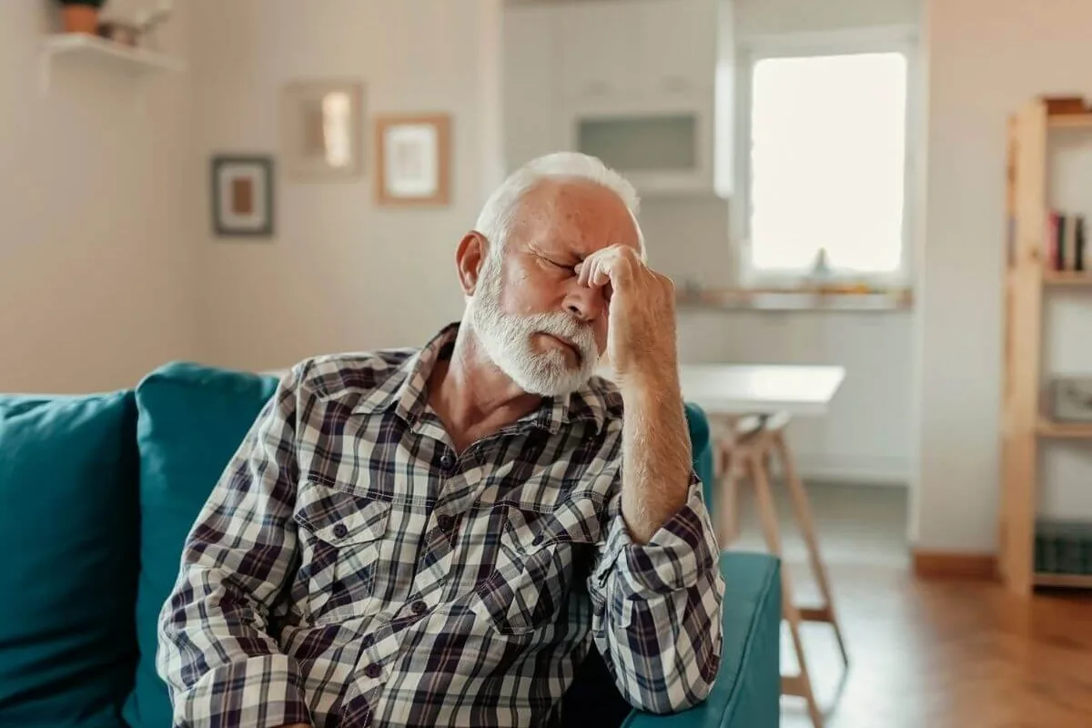 An older man on a sofa pinching the bridge of his nose