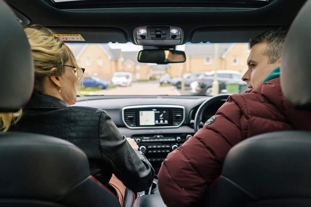 A couple seen from the back seat of a car, the woman driving
