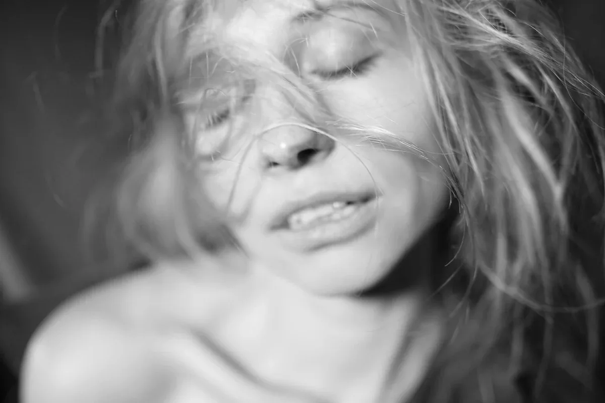Black-and-white close-up of a woman with her eyes closed and hair across her face, smiling softly
