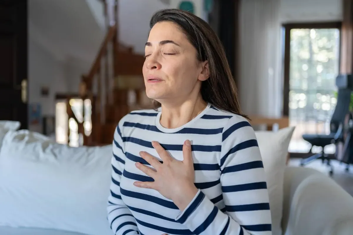 A woman with her eyes closed and a hand on her chest, breathing slowly at home