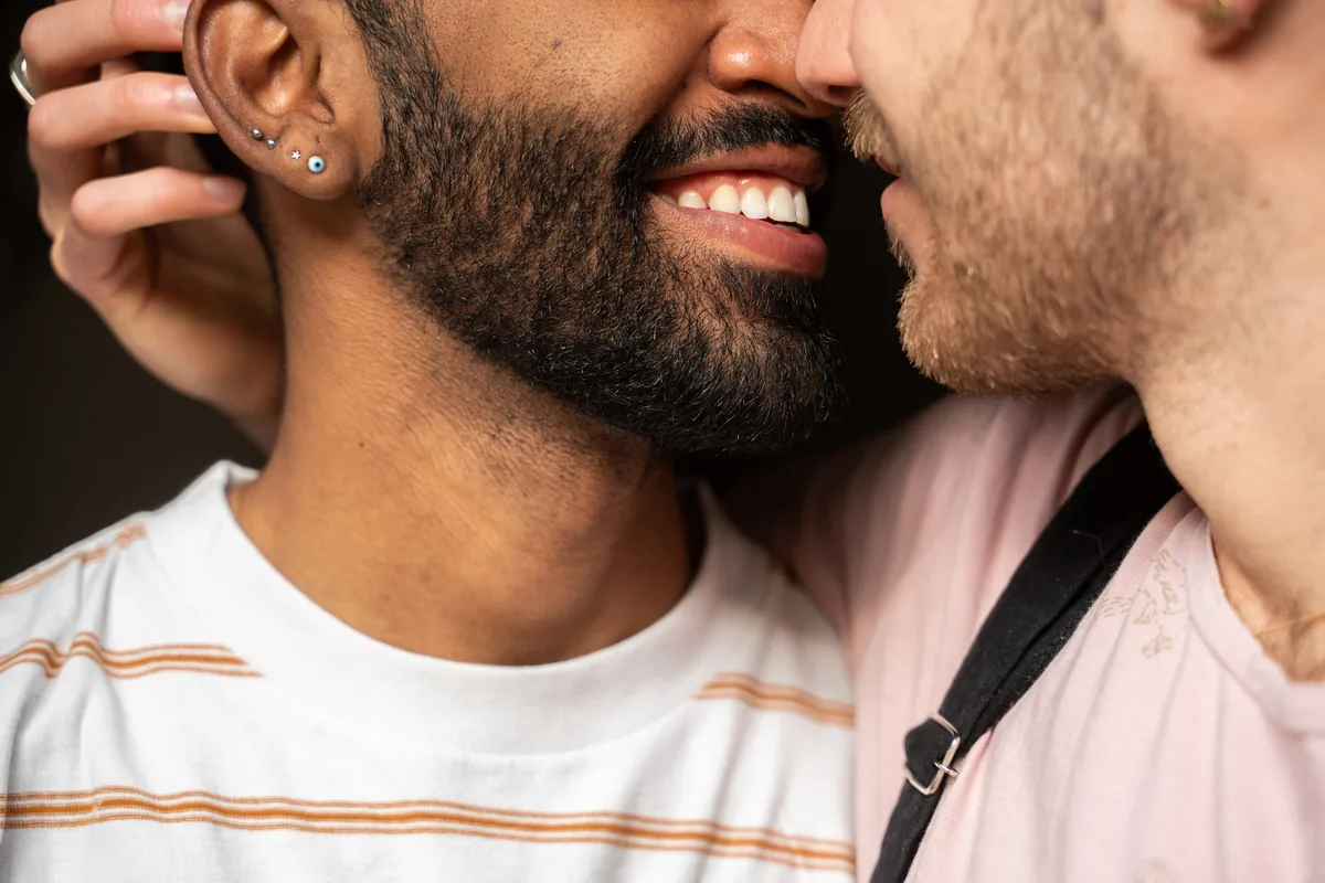 Two men with their faces close together in a tender moment, one smiling widely as the other cradles his head