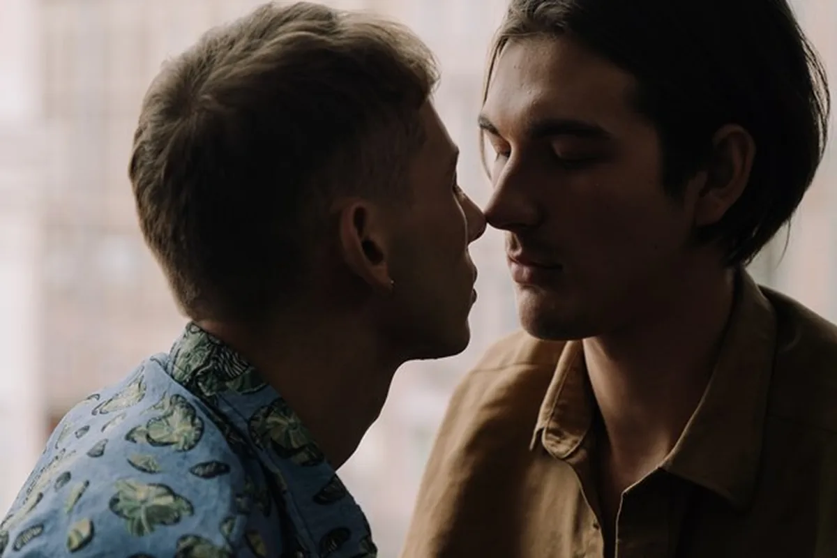 Two men standing close by a window, foreheads nearly touching