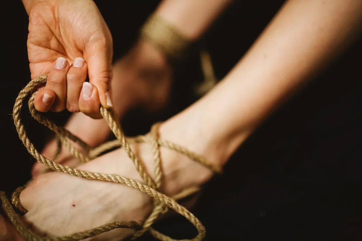 A hand holding natural-fiber rope loosely tied around an ankle