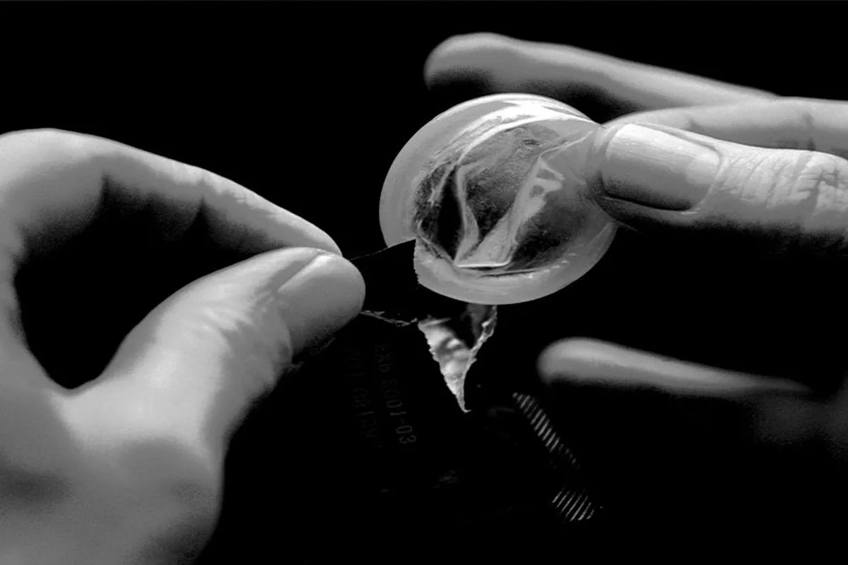 Black-and-white photo of two hands tearing open an unbranded foil condom wrapper