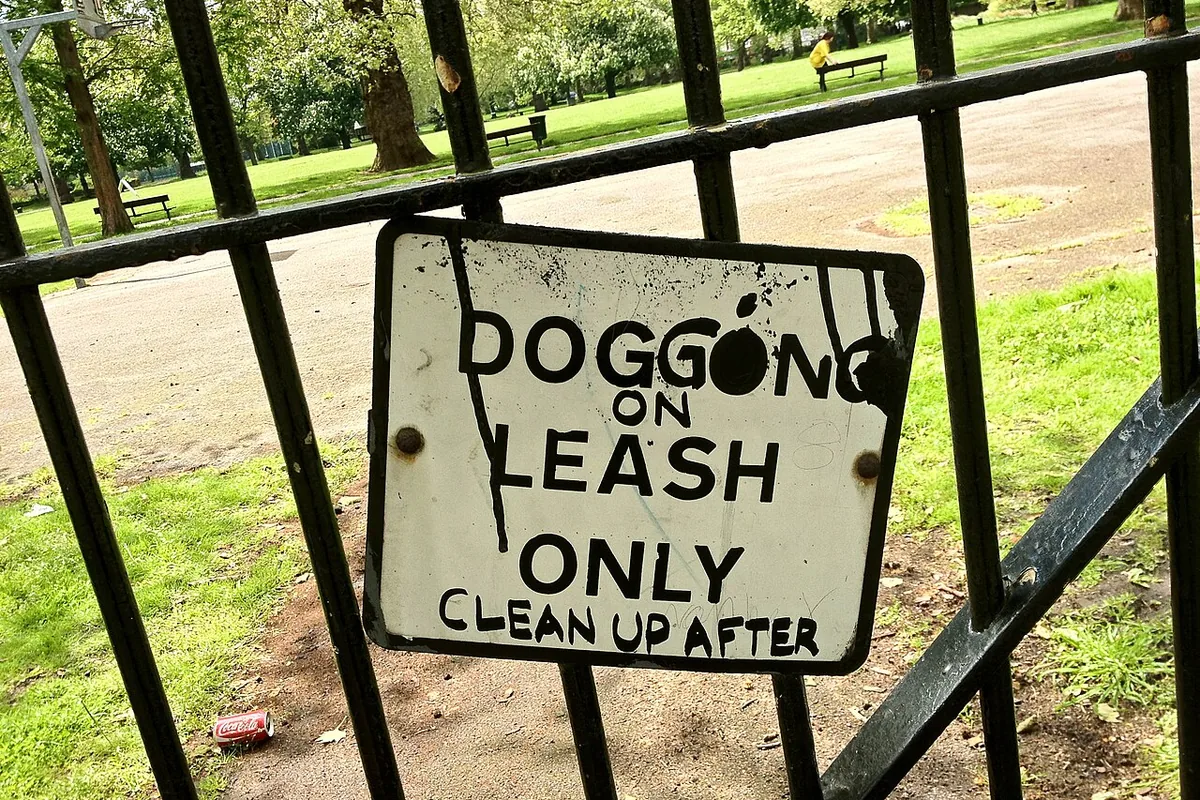 A hand-painted park sign on a railing about keeping dogs on a leash