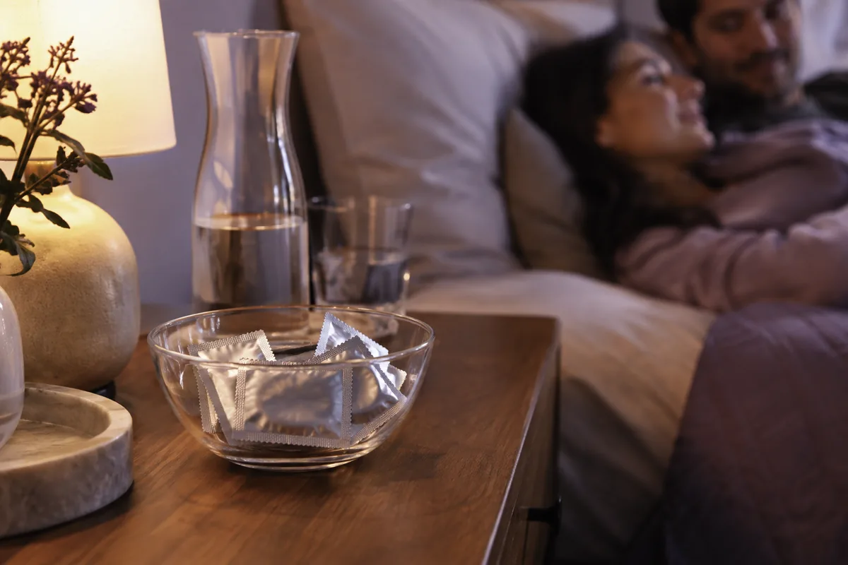 A glass bowl of wrapped condoms on a bedside table