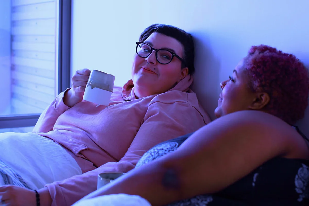 Two people relaxing together in bed with mugs of tea