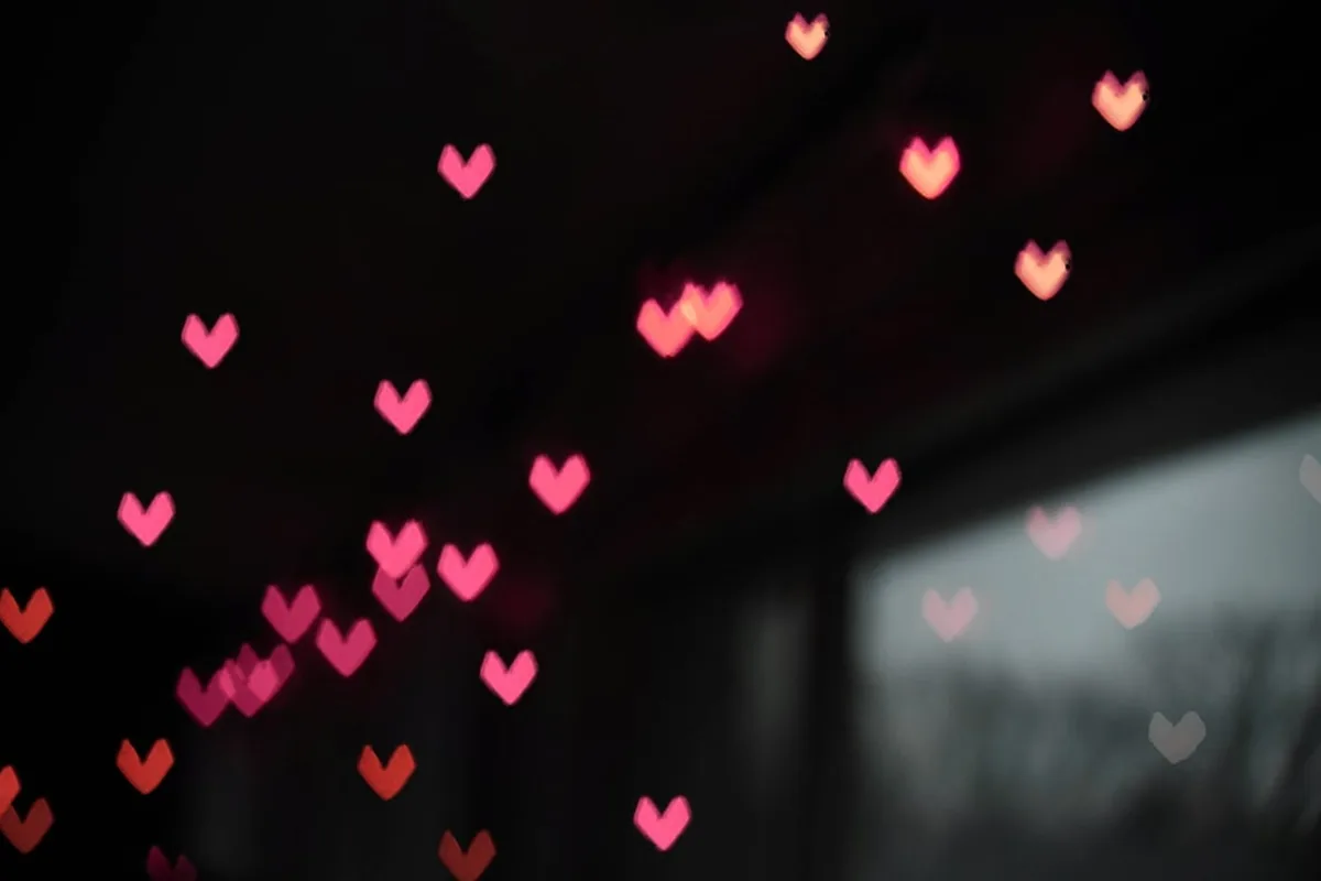 Heart-shaped bokeh lights glowing in pink, red and orange tones against a dark background