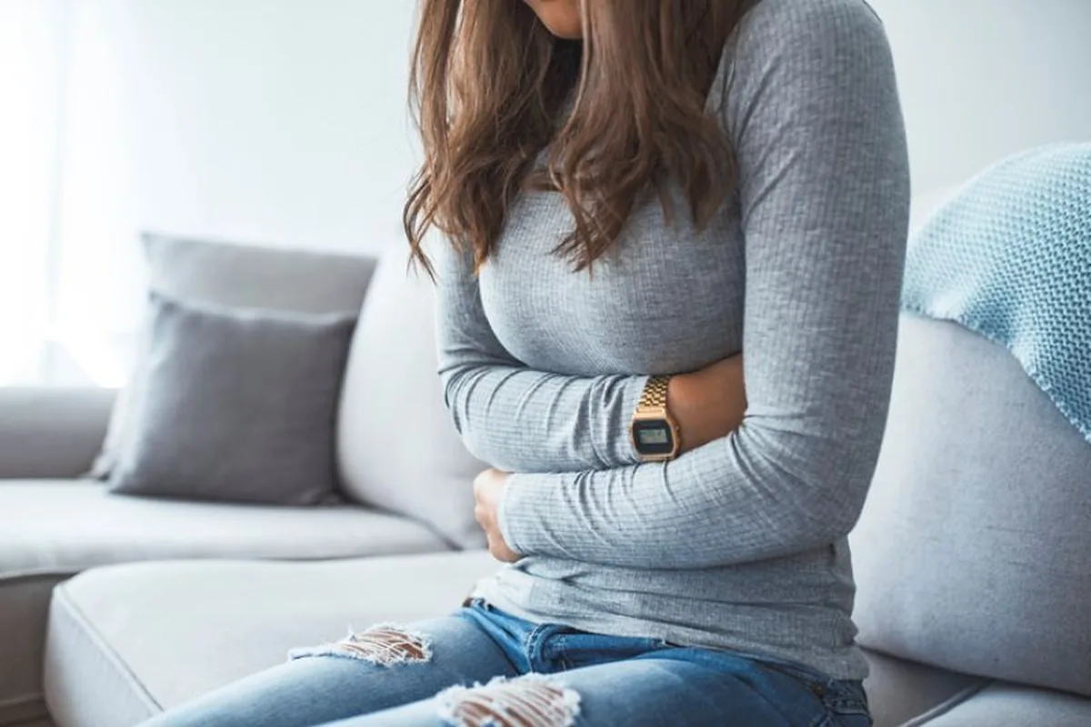 A woman sitting on a sofa holding her stomach in discomfort