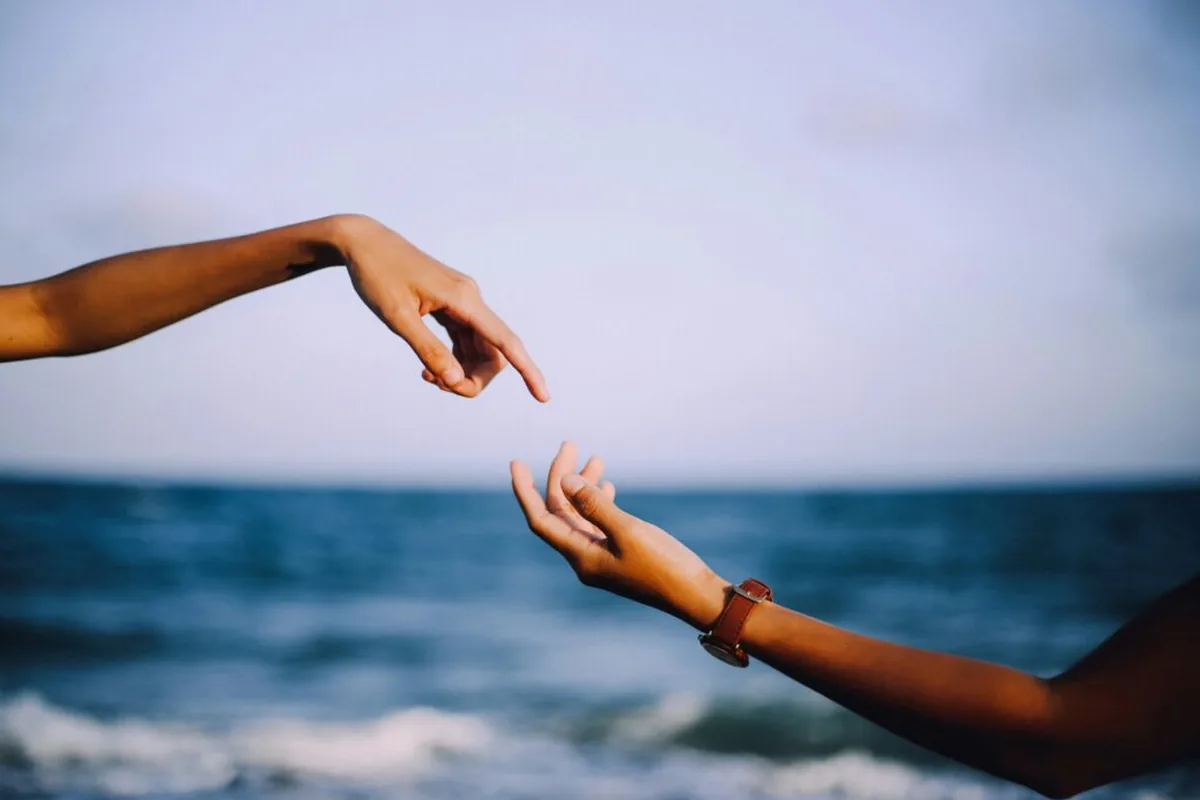 Two hands reaching toward each other over the sea
