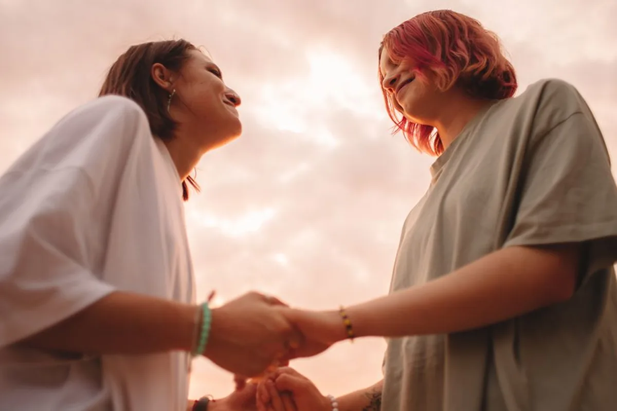 Two people holding both hands and smiling at sunset