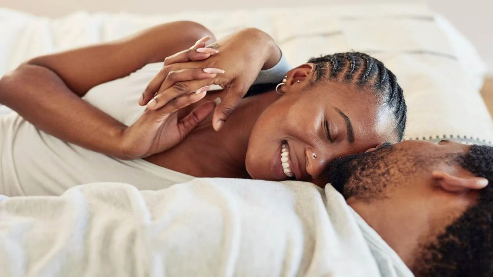 A couple lying in bed laughing together, holding hands