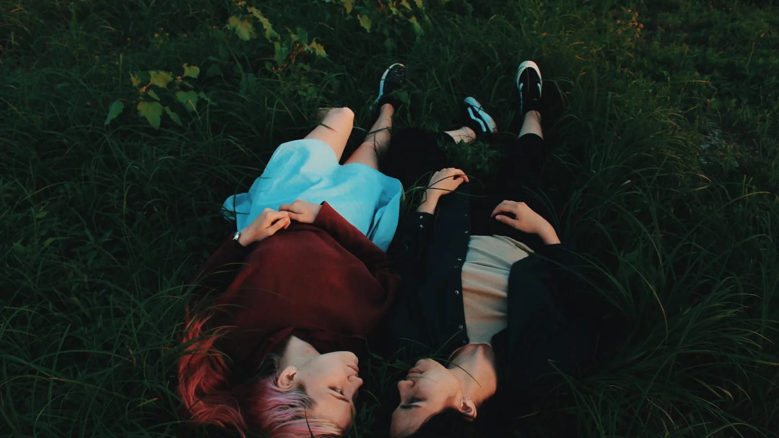 Two women lying head to head in the grass at dusk