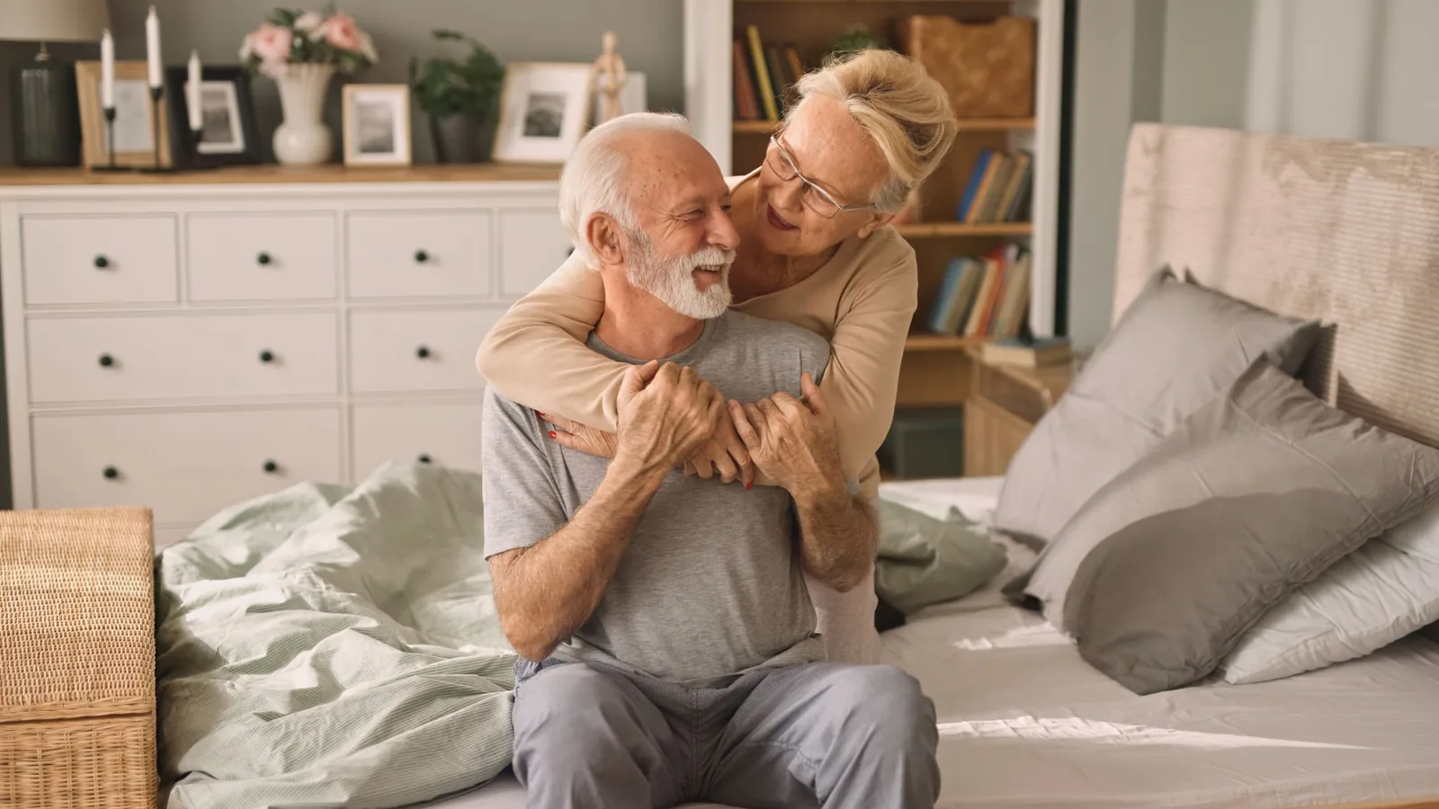 An older couple hugging and smiling on the edge of their bed